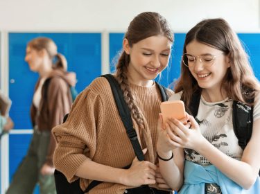 Zwei junge Mädchen schauen zusammen auf ein Smartphone.