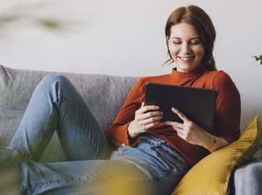 Eine Frau sitzt auf einem Sofa und benutzt ein Tablet.