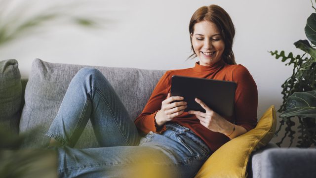Eine Frau sitzt auf einem Sofa und benutzt ein Tablet.