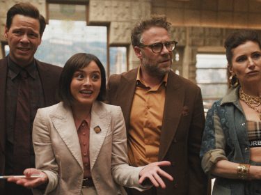 Auf dem Bild in dem Artikel zu The Studio Ende erklärt sind vier Charaktere zu sehen. Sie stehen in einem Raum. Die Figur ganz links wirkt skeptisch, daneben steht eine Frau im cremefarbenen Anzug, die lebhaft gestikuliert. Rechts daneben ein Mann mit Brille und orangefarbenem Hemd, der aufmerksam schaut. Ganz rechts steht eine Frau mit goldenen Ketten und großen Creolen, die selbstbewusst und leicht herausfordernd wirkt.