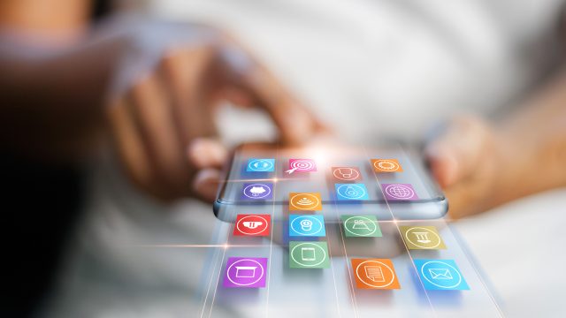 Eine Frau hält ein Smartphone in der Hand und wischt scheinbar App-Icons aus dem Gerät heraus.