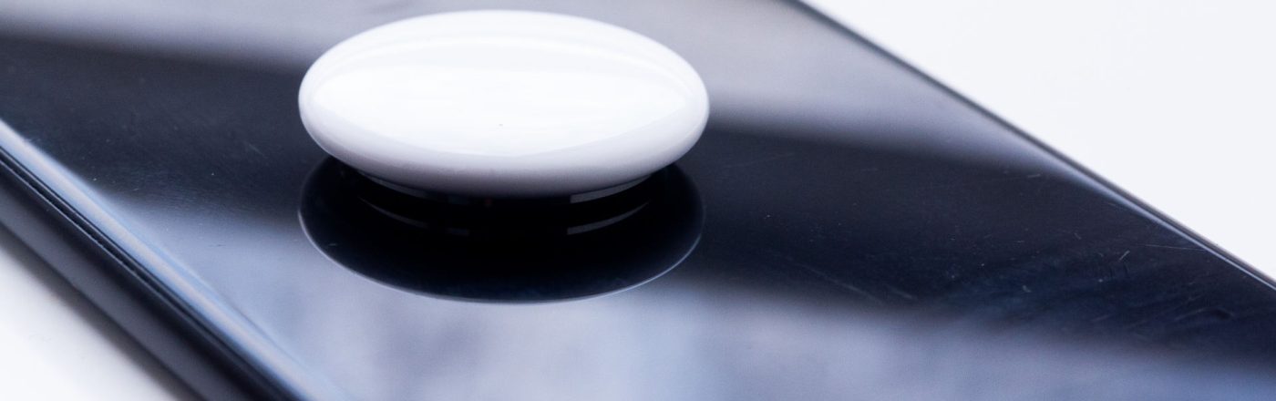 Ein weißer, runder Bluetooth-Tracker liegt auf einem schwarzen Smartphone.