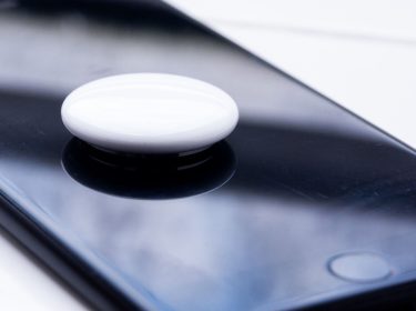 Ein weißer, runder Bluetooth-Tracker liegt auf einem schwarzen Smartphone.