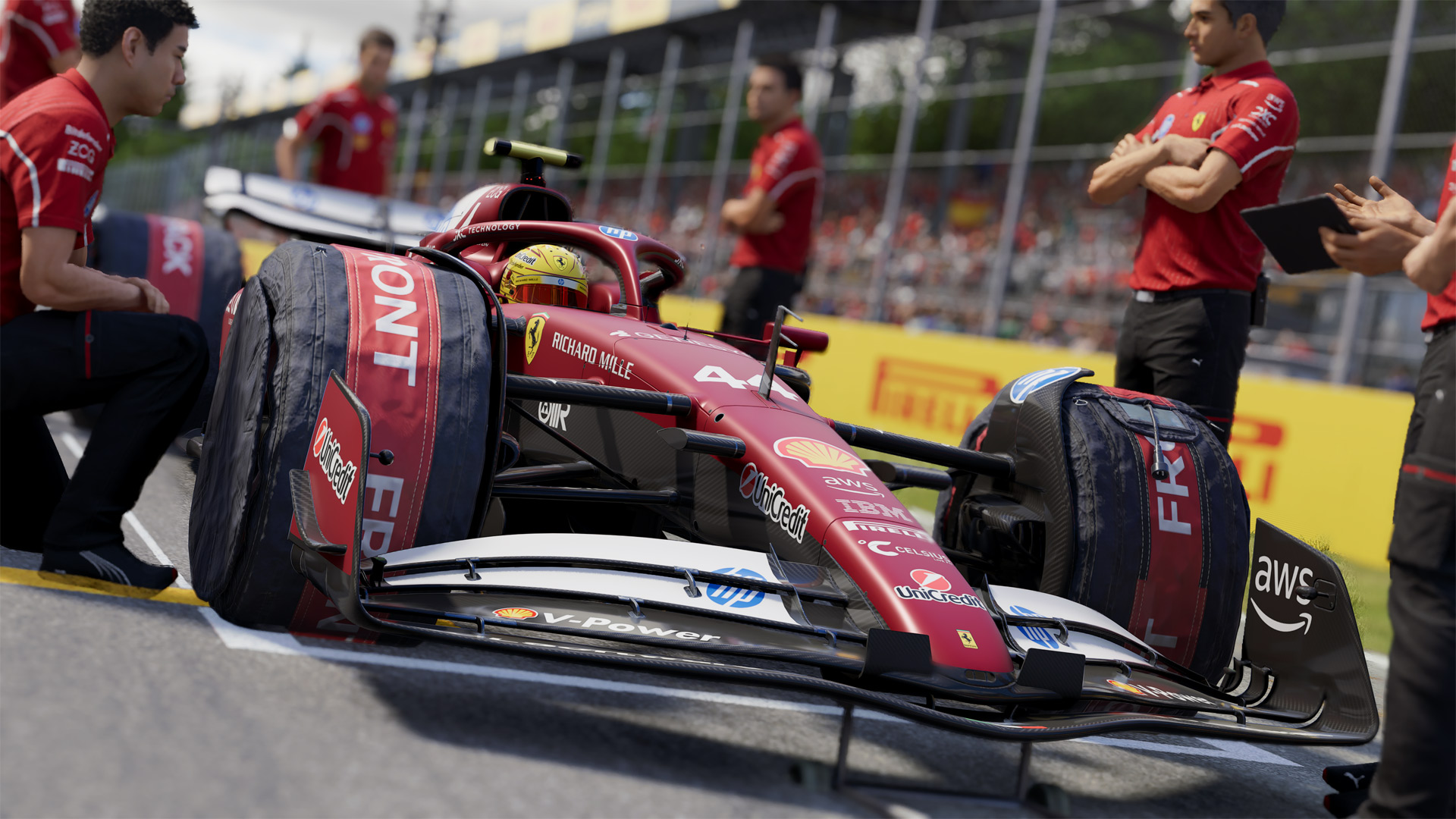 Im Bild zum F1 25 Test steht Lewis Hamilton in seinem Ferrari-Wagen an der Boxengasse, umgeben von seinem virtuellen Team. Der Formel-1-Bolide ist mit Reifenschonern ausgestattet und zeigt Sponsoren wie Shell, HP und AWS. Hamiltons goldener Helm ist gut sichtbar, die Szene wirkt gespannt und detailreich.