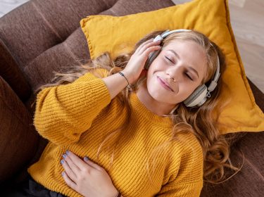 Eine Frau liegt auf dem Sofa und hört Musik.