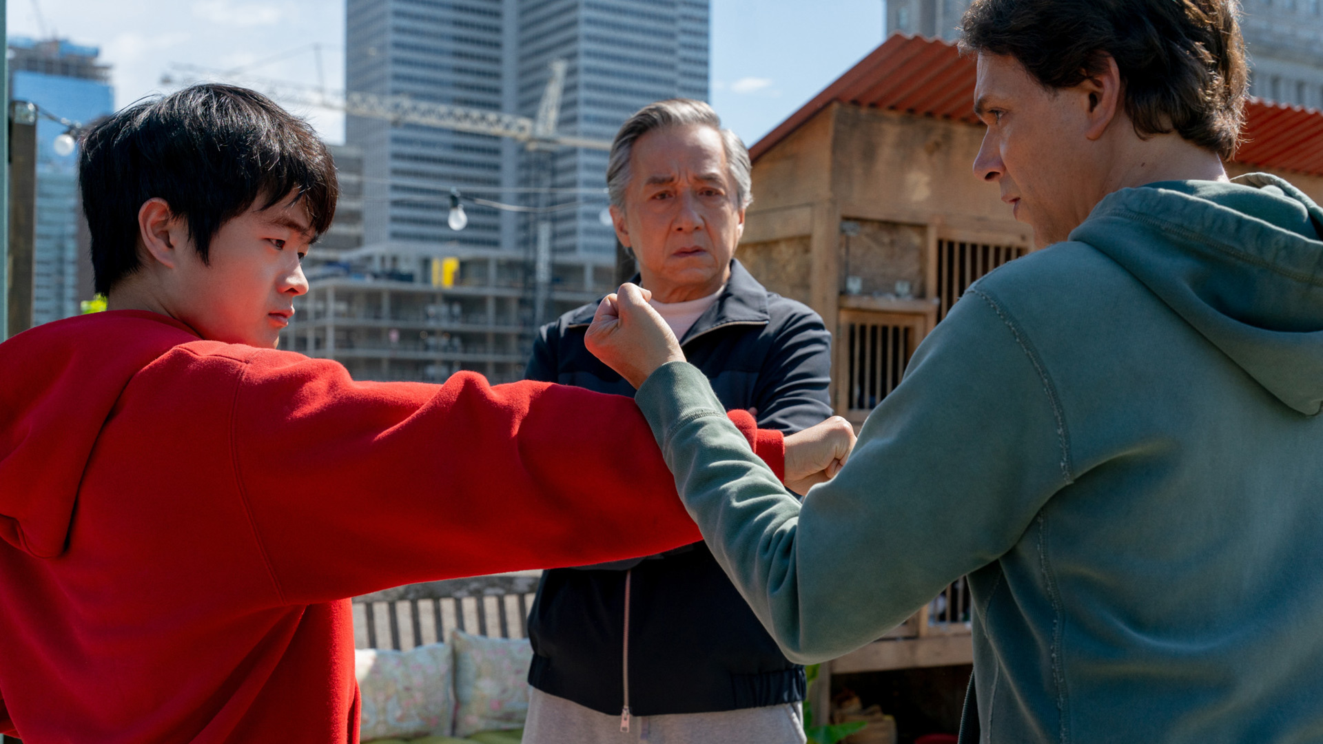 In dieser Szene aus Karate Kid: Legends stehen sich Ben Wang als Li Fong und Ralph Macchio in einer Trainingshaltung gegenüber, während Jackie Chan konzentriert zwischen ihnen steht. Alle drei tragen Freizeitkleidung. Die Szene wirkt intensiv und lehrreich – ein zentrales Motiv für die Karate Kid: Legends Kritik.