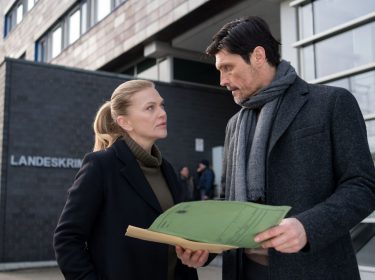 Die zwei Schauspieler Anna Loos und Stipe Erceg stehen vor dem Landeskriminalakt und schauen in eine Akte.
