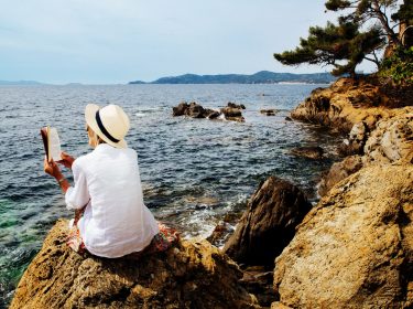 Eine Frau liest an einer felsigen Küste ein Buch