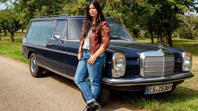 Anna Fischer lehnt in einer Szene von "Die Bestatterin" an einem Leichenwagen.