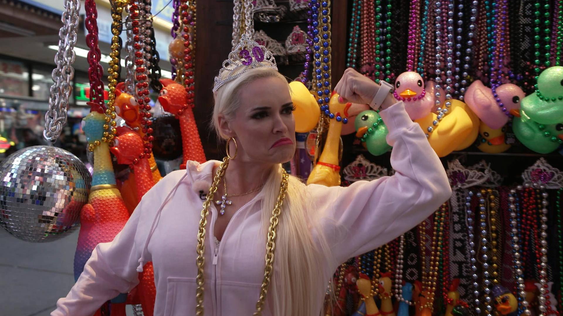 Im Bild in den GigaTV-Highlights im Juni 2025 ist Daniela Katzenberger in einer Szene aus Staffel 2 ihrer gleichnamigen Reality-Serie zu sehen. Sie trägt eine pinke Kapuzenjacke, eine Tiara mit der Aufschrift „30“ und eine goldene Kette, während sie selbstbewusst vor einer Wand aus Gummienten und bunten Perlenketten ihren Bizeps anspannt.