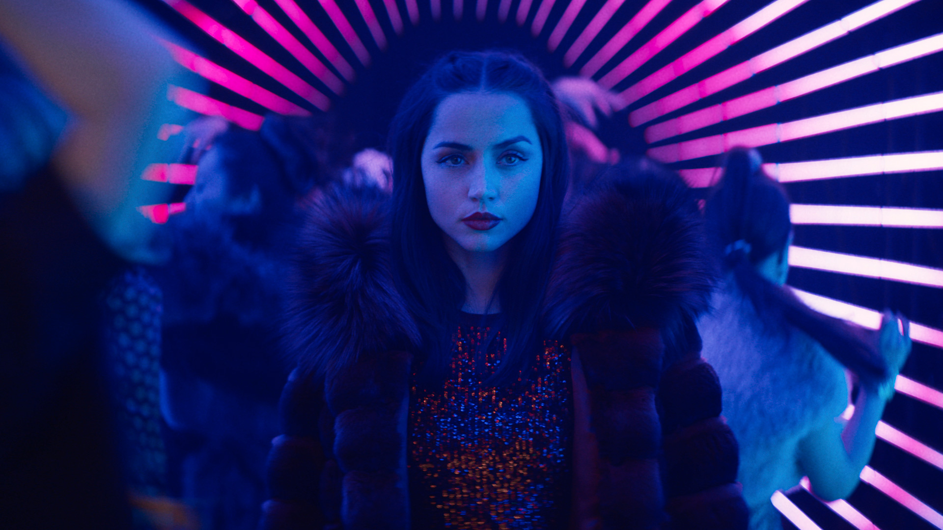 Im Bild zur John Wick Ballerina Kritik steht Ana de Armas als Eve selbstbewusst im Zentrum eines neonbeleuchteten Gangs. Sie trägt einen eleganten, mit Pelz besetzten Mantel und ein glitzerndes Kleid, während violette und blaue Lichtstreifen den Hintergrund rhythmisch betonen. Ihr direkter Blick vermittelt Entschlossenheit und Stärke inmitten einer pulsierenden Clubatmosphäre.