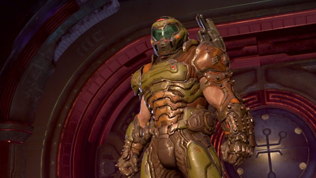Auf dem Bild zur Doom Reihenfolge ist der Doom Slayer aus dem Spiel Doom Eternal zu sehen. Er trägt eine schwer gepanzerte grün-bronzene Rüstung mit Helm und steht in einer futuristischen, rot beleuchteten Umgebung.