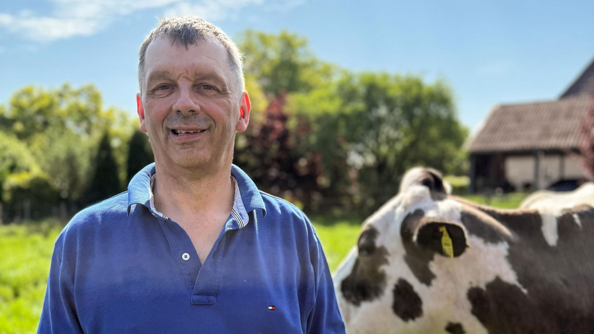 Bei Bauer sucht Frau 2025 steht Kandidat Johann in blauem Poloshirt auf einer Weide. Hinter ihm grast eine Kuh, während er in ländlicher Idylle entspannt in die Kamera lächelt.
