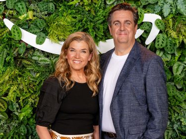 Auf dem Bild in dem Artikel zu Perfekt zusammen stehen Anke Engelke und Bastian Pastewka nebeneinander vor einer grünen Pflanzenwand und lächeln in die Kamera. Anke Engelke trägt ein schwarzes Oberteil und gemusterten Rock, während Bastian Pastewka ein weißes T-Shirt unter einem blauen Sakko trägt.