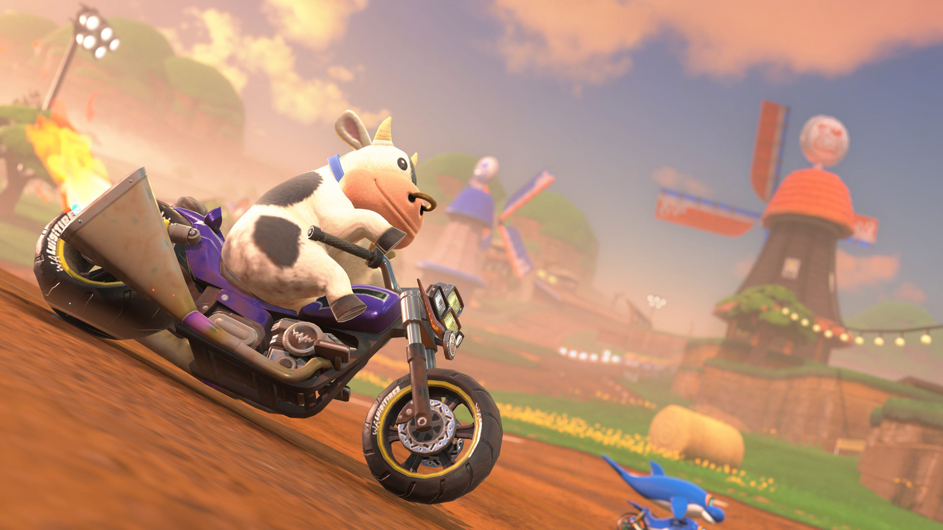 Im Bild zu Mario Kart World Tipps fährt eine schwarz-weiße Kuh als spielbarer Charakter auf einem violetten Motorrad durch eine ländliche Strecke mit Windmühlen, Feldern und Strohballen. Der Himmel ist in warmes Licht getaucht und vermittelt eine verspielte, fast absurde Atmosphäre – typisch für die kreativen Kurse von Mario Kart.