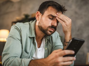 Ein Mann schaut genervt auf sein Smartphone und fasst sich an die Stirn.