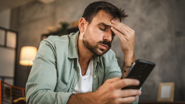 Ein Mann schaut genervt auf sein Smartphone und fasst sich an die Stirn.