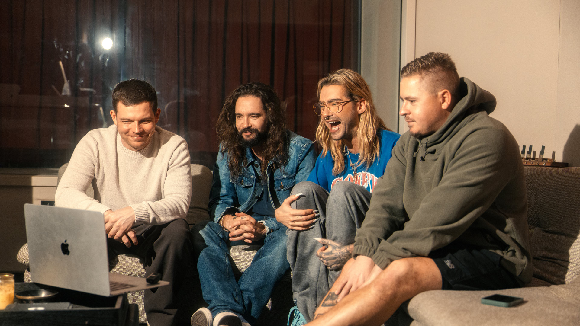 Auf dem Bild zur Kaulitz & Kaulitz Staffel 3 sitzen Bill und Tom Kaulitz gemeinsam mit Georg und Gustav von Tokio Hotel auf einem Sofa. Sie schauen lachend und konzentriert auf einen Laptop-Bildschirm, vermutlich während eines Online-Calls oder einer Besprechung. Die Atmosphäre wirkt freundschaftlich, kreativ und entspannt – ein möglicher Blick hinter die Kulissen.