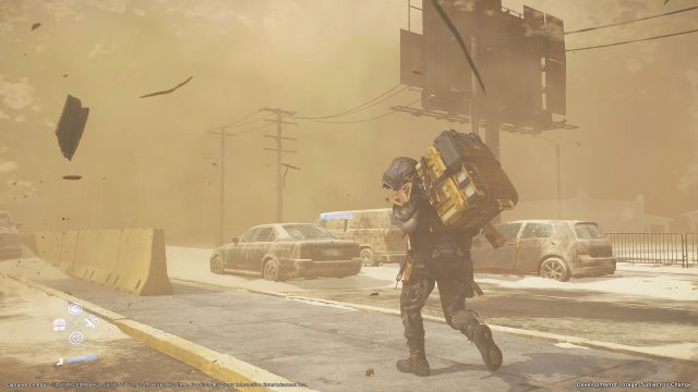 Auf diesem Screenshot aus Death Stranding 2: On the Beach kämpft der Lieferant in schwerer Ausrüstung gegen einen heftigen Sandsturm an. Er geht gebückt und schützt sein Gesicht, während hinter ihm verlassene, verrostete Autos und eine staubige Straße eine postapokalyptische Stimmung erzeugen.