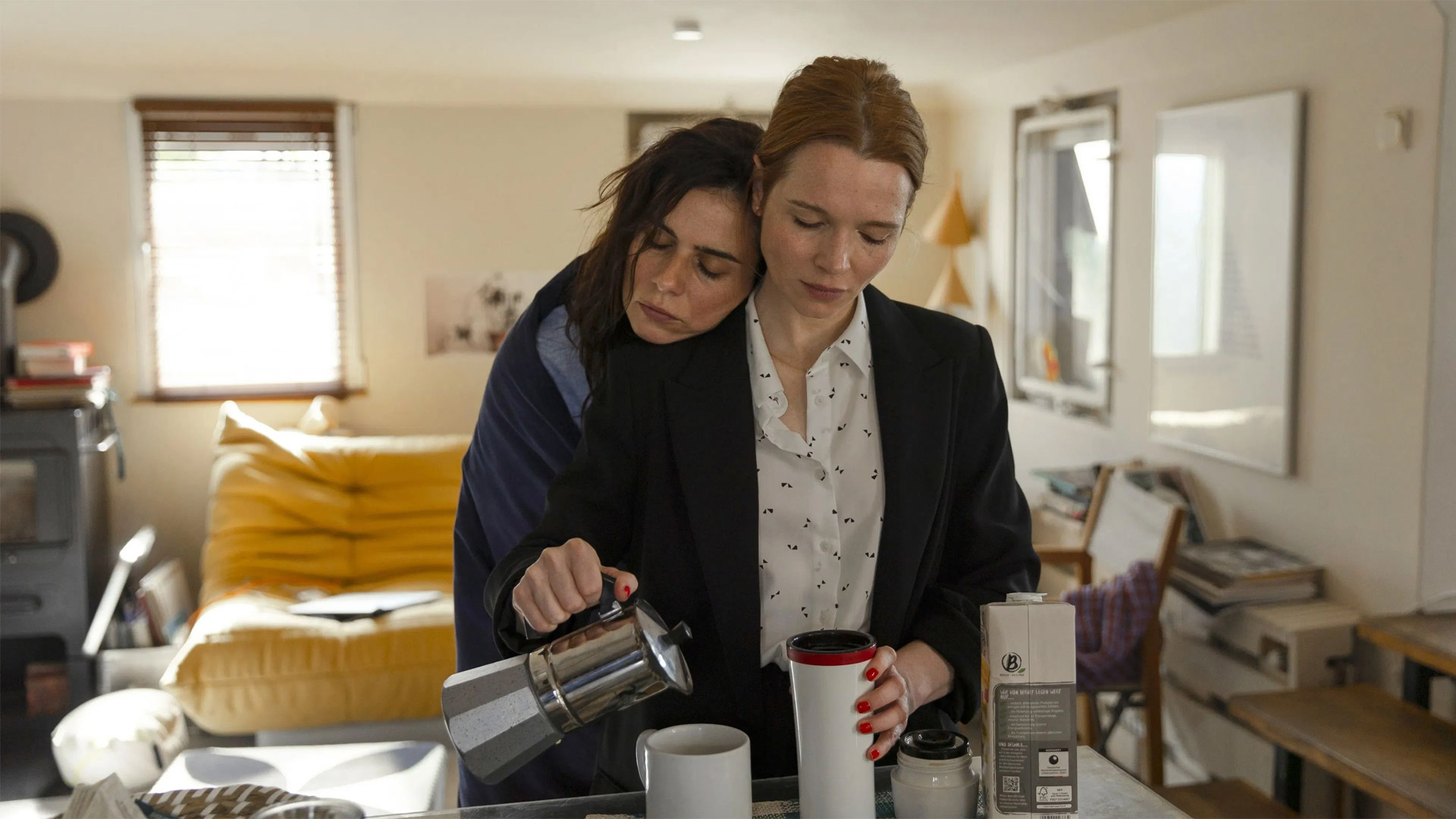 In den GigaTV-Highlights im Juli 2025 siehst du ein Bild aus dem Film Wunderschöner: Karoline Herfurth als Sonja steht in einer Küche und gießt Kaffee aus einer Kanne in einen Becher. Hinter ihr lehnt Nora Tschirner als Vicky mit geschlossenen Augen und dem Kopf auf Sonjas Schulter
