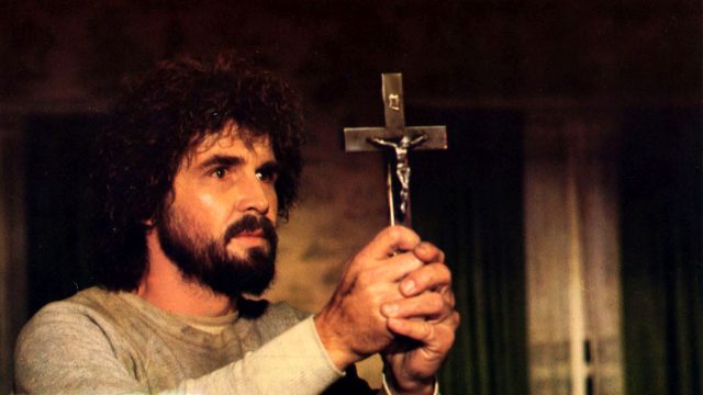 Schauspieler James Brolin hält im Film "Amityville Horror" ein Kruzifix hoch.