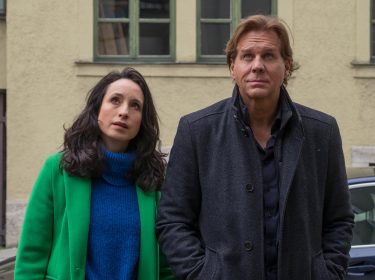 Das Artikelbild zu den Der Alte-Darsteller:innen zeigt Thomas Heinze als Hauptkommissar Caspar Bergmann (rechts) und Stephanie Stumph als Kommissarin Annabell Lorenz (links) nebeneinander in einem Innenhof. Beide blicken nachdenklich nach oben. Heinze trägt einen dunklen Mantel, Stumph einen auffälligen grünen Mantel über einem blauen Pullover.
