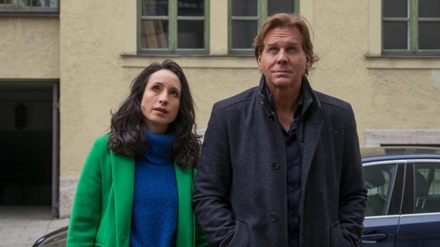 Das Artikelbild zu den Der Alte-Darsteller:innen zeigt Thomas Heinze als Hauptkommissar Caspar Bergmann (rechts) und Stephanie Stumph als Kommissarin Annabell Lorenz (links) nebeneinander in einem Innenhof. Beide blicken nachdenklich nach oben. Heinze trägt einen dunklen Mantel, Stumph einen auffälligen grünen Mantel über einem blauen Pullover.
