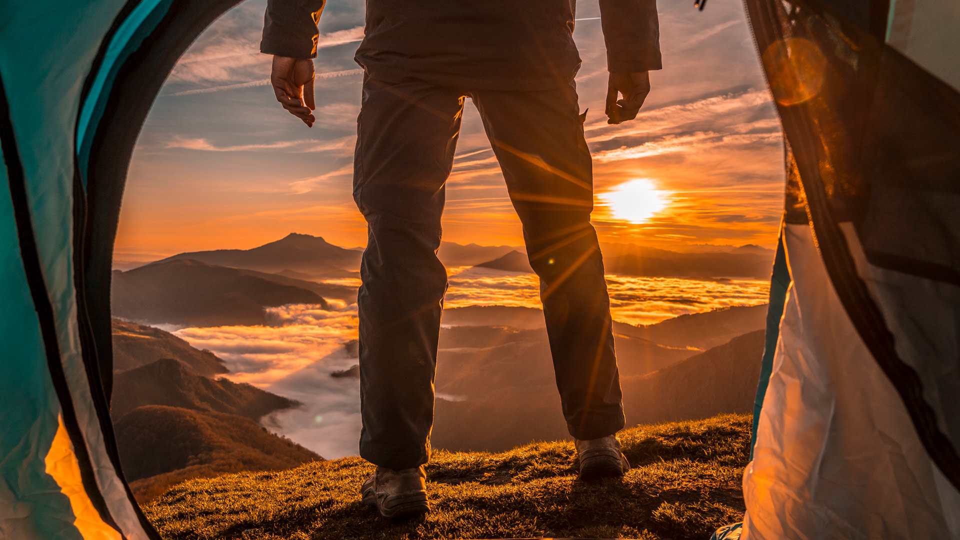 Das Bild aus der GO Real Life-Kampagne zeigt den Blick aus einem geöffneten Zelt auf eine atemberaubende Berglandschaft im Sonnenaufgang. Im Vordergrund steht eine Person in Outdoor-Kleidung mit Blick auf ein wolkenverhangenes Tal. Die Szene symbolisiert Freiheit, Abenteuerlust und die Nähe zur Natur.