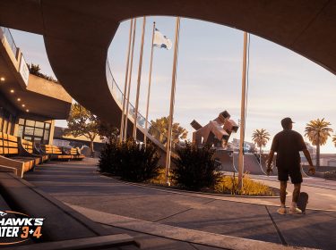 Auf dem Bild in dem Artikel zu den Tony Hawk’s Pro Skater 3 + 4 Tipps steht ein Skater mit Skateboard in der Hand in einem sonnigen Skatepark. Im Hintergrund sind Palmen, moderne Architektur und eine große Halfpipe zu sehen.