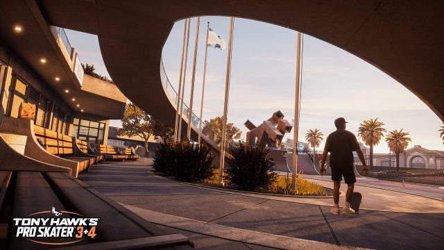 Auf dem Bild in dem Artikel zu den Tony Hawk’s Pro Skater 3 + 4 Tipps steht ein Skater mit Skateboard in der Hand in einem sonnigen Skatepark. Im Hintergrund sind Palmen, moderne Architektur und eine große Halfpipe zu sehen.
