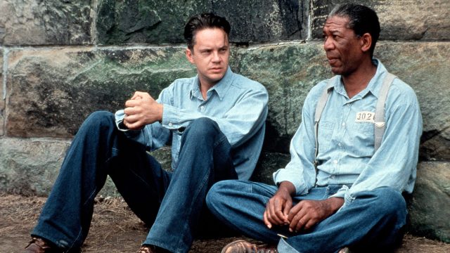 Auf dem Bild in dem Artikel zu den besten Filmen laut IMDb sitzen zwei Menschen in blauen Uniformen an einer Mauer. Die Szene stammt aus dem Filmklassiker „Die Verurteilten“.
