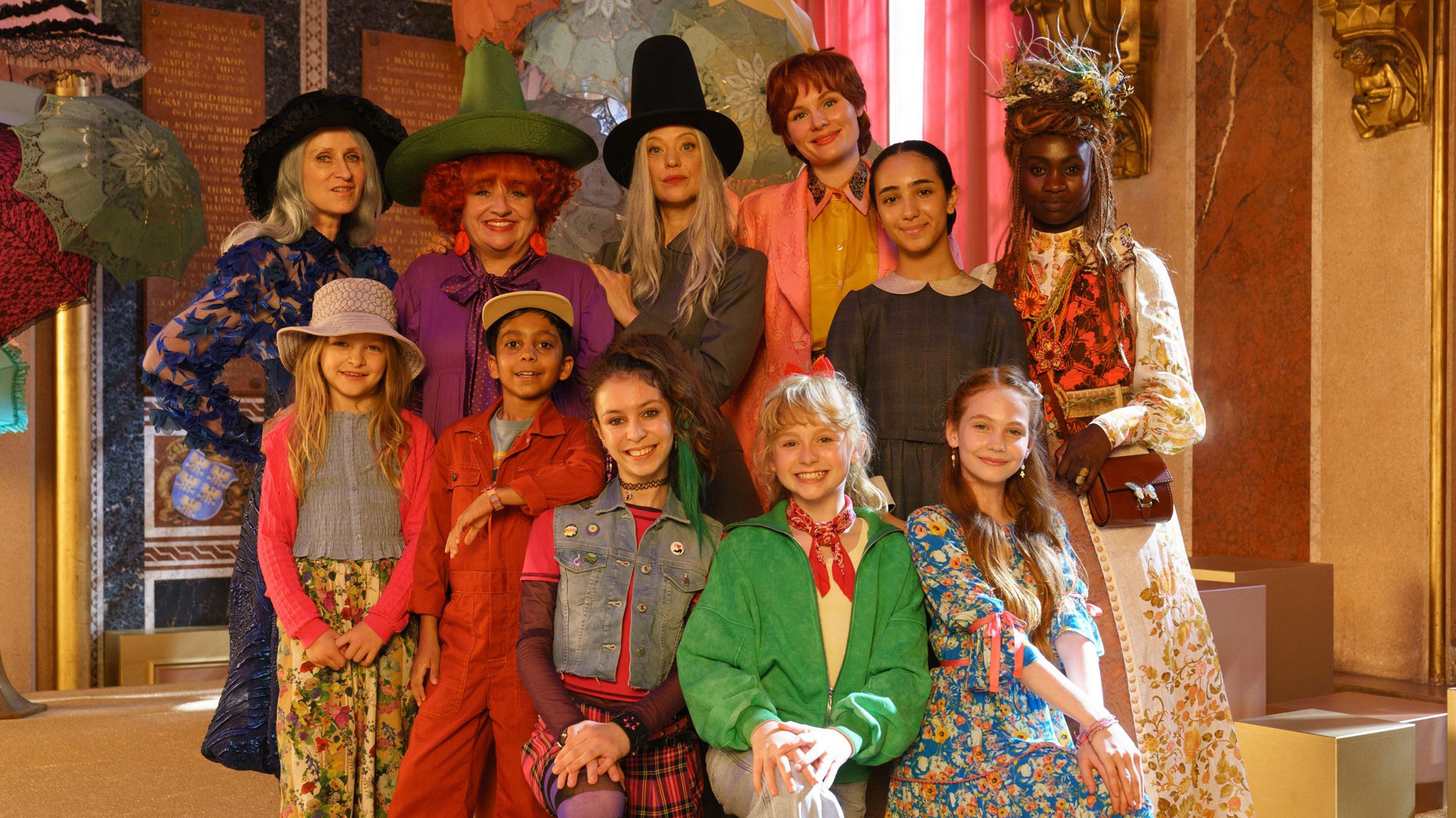 Auf dem Bild zu Bibi Blocksberg – Das große Hexentreffen posieren elf Personen in einem festlich geschmückten Saal. In der hinteren Reihe stehen Sophie Rois, Maria Happel, Heike Makatsch, Rosalie Thomass, Shanti Celik und Lorna Ishema in fantasievollen, hexenhaften Kostümen. Davor sitzen oder stehen Gwen-Ewa Makatsch, Balthazar Gyan Alexis, Carla Demmin, NALA und Philomena Amari fröhlich lächelnd in farbenfroher Kleidung. Die Stimmung ist lebhaft und verspielt.
