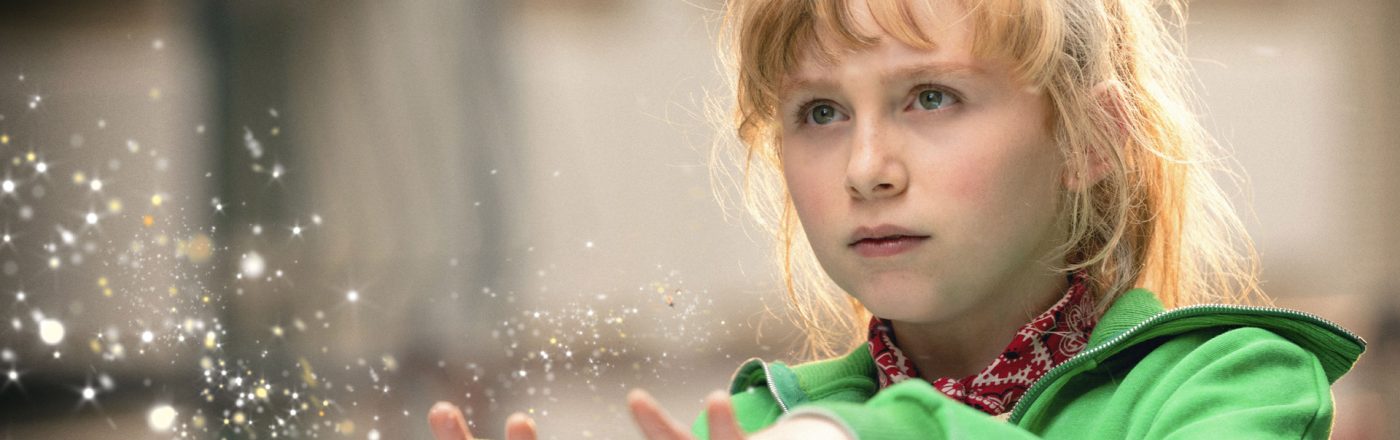 In dieser Szene aus Bibi Blocksberg – Das große Hexentreffen ist NALA als Bibi Blocksberg zu sehen. Sie trägt eine grüne Jacke und ein rotes Haarband, während sie konzentriert mit ausgestreckten Händen magische Funken erzeugt. Die Lichtpartikel unterstreichen die zauberhafte Stimmung und Bibis Entschlossenheit in einem wichtigen Moment.