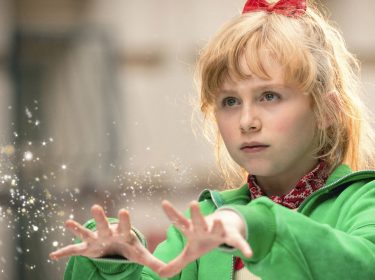 In dieser Szene aus Bibi Blocksberg – Das große Hexentreffen ist NALA als Bibi Blocksberg zu sehen. Sie trägt eine grüne Jacke und ein rotes Haarband, während sie konzentriert mit ausgestreckten Händen magische Funken erzeugt. Die Lichtpartikel unterstreichen die zauberhafte Stimmung und Bibis Entschlossenheit in einem wichtigen Moment.