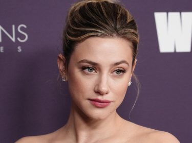Auf dem Bild in dem Artikel zum The Love Hypothesis-Film ist Lili Reinhart vor einer violetten Pressewand zu sehen. Sie blickt leicht zur Seite