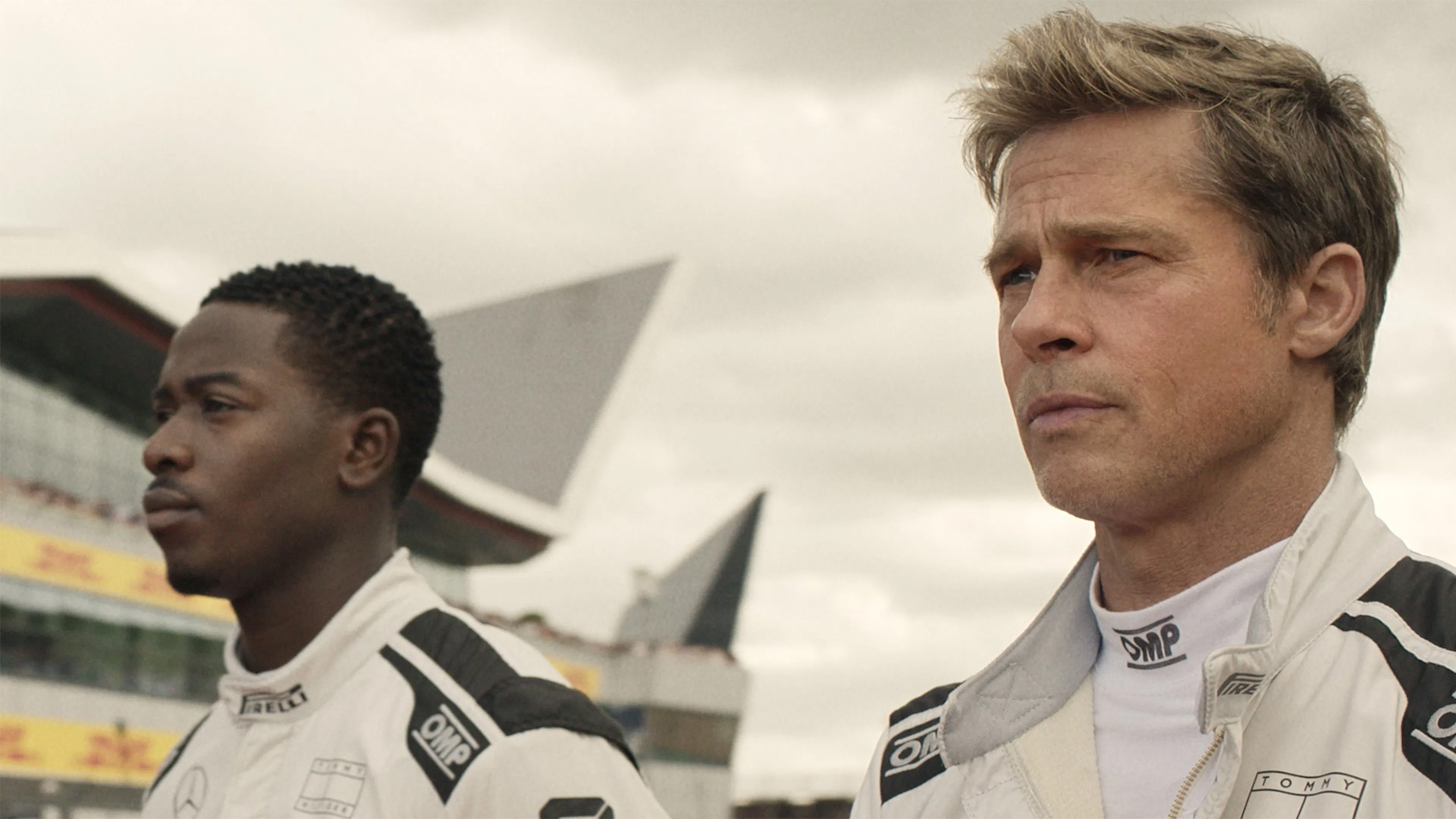 In den GigaTV-Highlights im August ist eine Szene aus dem Film F1 zu sehen, in der Brad Pitt als Ex-Rennprofi in einem weißen Rennanzug neben einem jungen Fahrer steht.