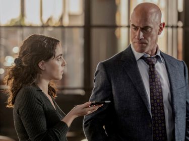 In den GigaTV-Highlights im August ist eine Szene aus Law and Order: Organized Crime zu sehen, in der Elliot Stabler, gespielt von Christopher Meloni, im Anzug einer jungen Frau mit Aufnahmegerät gegenübersteht.
