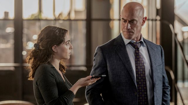 In den GigaTV-Highlights im August ist eine Szene aus Law and Order: Organized Crime zu sehen, in der Elliot Stabler, gespielt von Christopher Meloni, im Anzug einer jungen Frau mit Aufnahmegerät gegenübersteht.