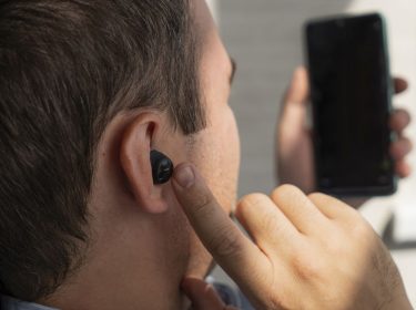 Ein Mann mit In-Ear-Kopfhörern im Ohr schaut auf sein Smartphone