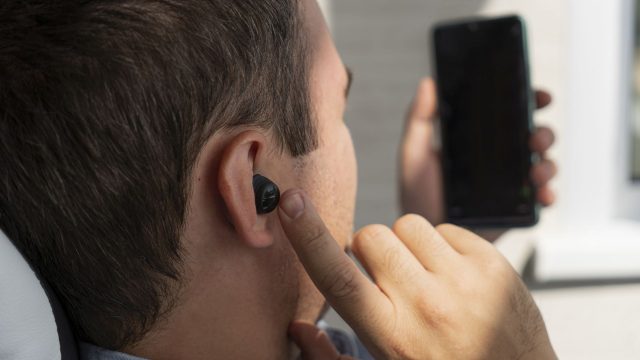 Ein Mann mit In-Ear-Kopfhörern im Ohr schaut auf sein Smartphone
