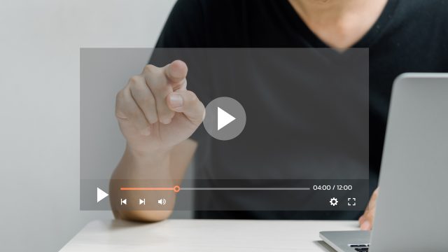 Ein Mann in schwarzem T-Shirt sitzt an einem Tisch und zeigt mit dem Finger auf einen transparent eingeblendeten Play-Button eines Videoplayers. Auf der rechten Seite ist ein aufgeklappter Laptop zu sehen. Das Bild symbolisiert die Nutzung eines digitalen Tools und steht stellvertretend für das Thema Sora Videos erstellen.