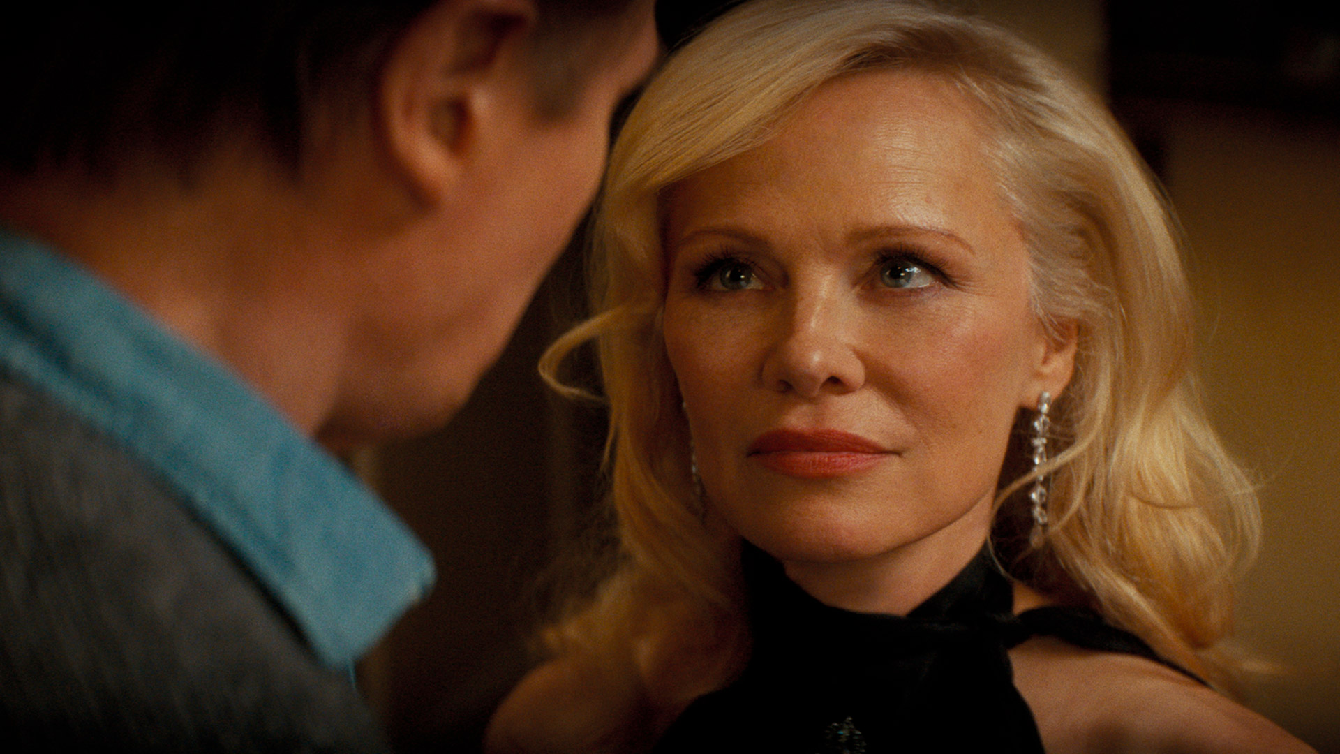 Pamela Anderson ist in ihrer Rolle als Beth in einer Nahaufnahme aus dem neuen Die nackte Kanone Film zu sehen. Ihr Blick ist ruhig, aber durchdringend, während sie einer männlichen Figur gegenübersteht. Mit eleganten Ohrringen, roten Lippen und einem schwarzen Kleid verkörpert sie Glamour und Geheimnis – passend zum humorvollen Ton von Die nackte Kanone.        ChatGPT fragen