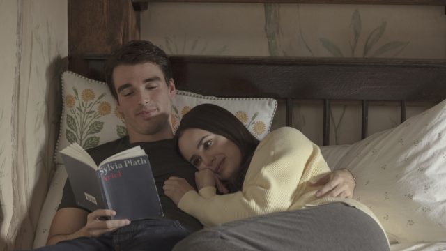 Sofia Carson und Corey Mychreest in My Oxford Year:Ein junges Paar liegt umschlungen auf einem Bett. Der Mann hält ein Buch, während sich die Frau an seine Schulter schmiegt.