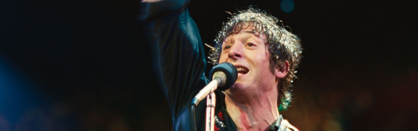 In Springsteen: Deliver Me From Nowhere steht Jeremy Allen White als Bruce Springsteen auf der Bühne, die rechte Faust triumphierend in die Luft gestreckt.