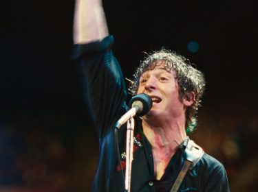 In Springsteen: Deliver Me From Nowhere steht Jeremy Allen White als Bruce Springsteen auf der Bühne, die rechte Faust triumphierend in die Luft gestreckt.