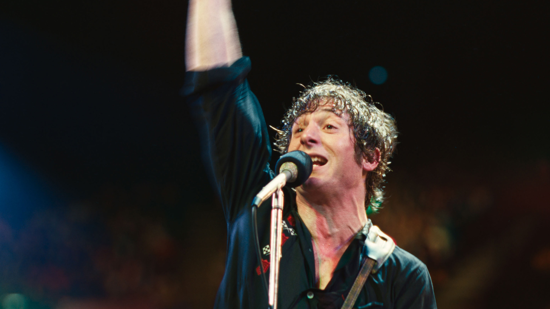 In Springsteen: Deliver Me From Nowhere steht Jeremy Allen White als Bruce Springsteen auf der Bühne, die rechte Faust triumphierend in die Luft gestreckt.