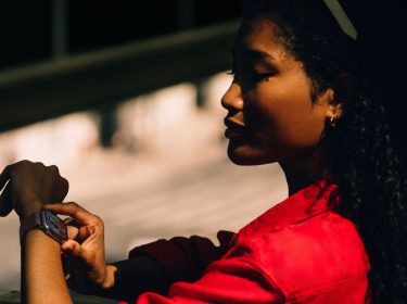 Frau mit rotem Hemd schaut auf ihre Apple Watch 11 am Handgelenk.