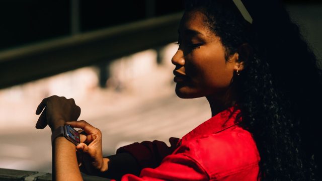 Frau mit rotem Hemd schaut auf ihre Apple Watch 11 am Handgelenk.