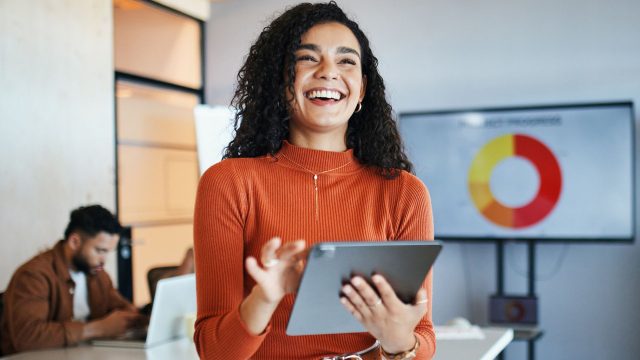 Junge Frau lächelt mit iPad in der Hand.