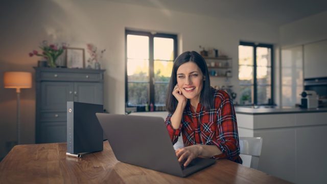 Router anschließen ohne Telefondose: Frau sitzt lächelnd vor einem Laptop.